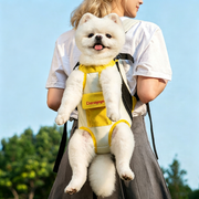 White Pomeranian sitting comfortably in DONOYOYO yellow and white pet carrier backpack worn by a woman outdoors, showing hands-free dog carrying in use