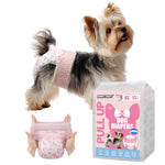 Yorkshire Terrier wearing Dono's Diary Pull Up female dog diaper in pink floral print, side view with tongue out; hands stretching open pink floral pull-up diaper showing elastic waistband; Dono's Diary Pull Up Dog Diapers XS 10pcs packaging, on white background