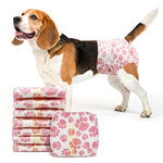 Beagle wearing Dono disposable pull-up female dog diaper in pink paw-print pattern, side view with mouth open, with stack of folded diapers showing yellow wetness indicator lines, on white background